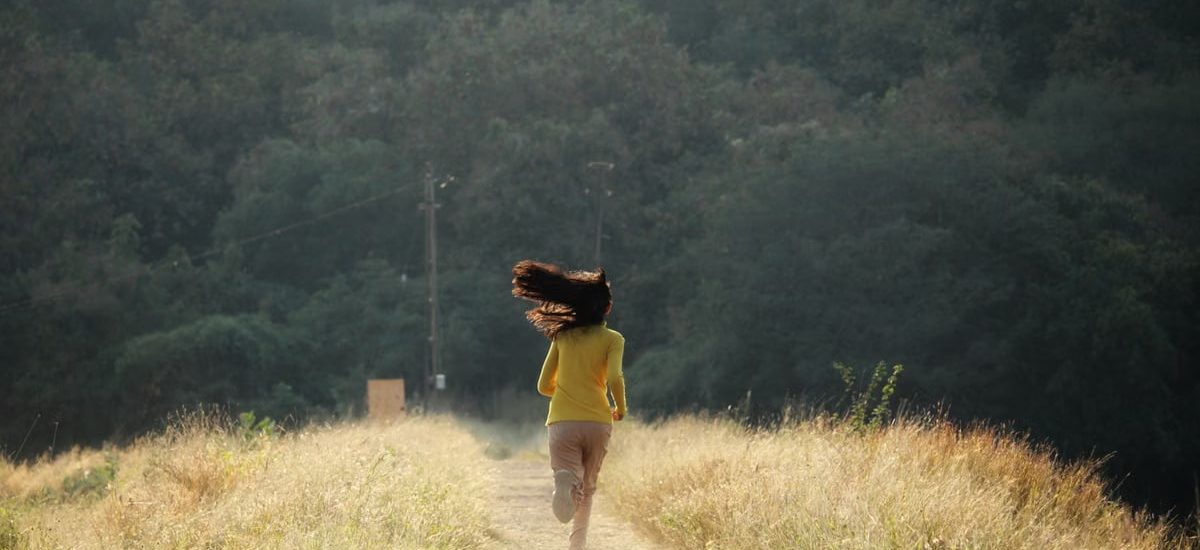 Young woman with long hair runs down a scenic path in summer. Embracing freedom and nature.